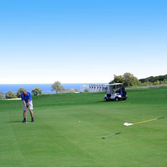 Mand spiller golf med blå himmel og Østersøen i baggrunden