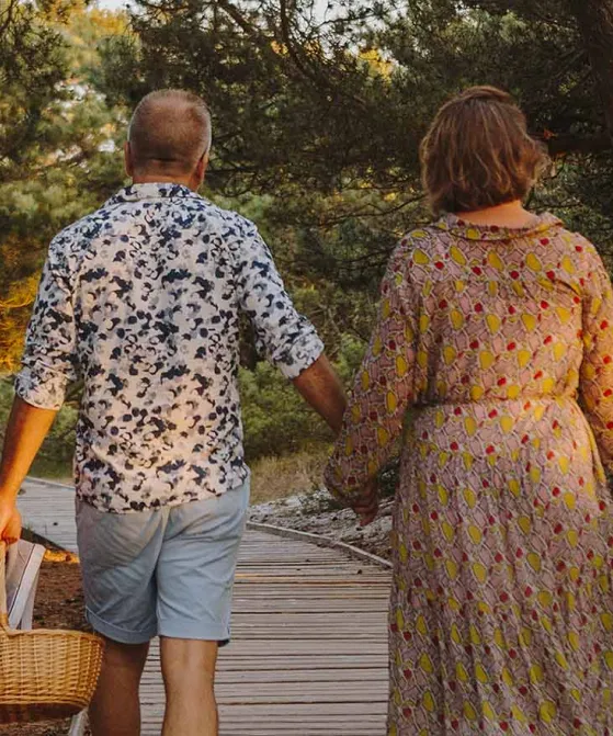 Par går hånd i hånd på sti med picnickurv