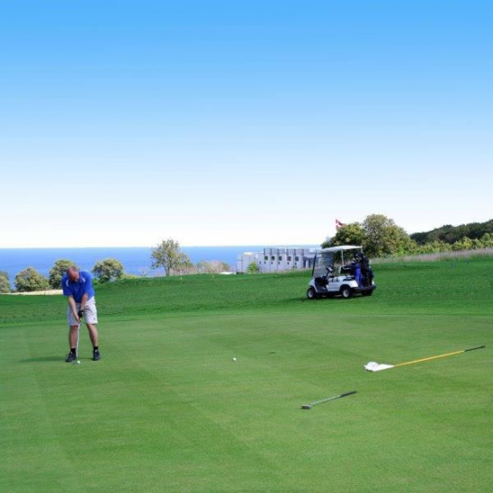 Mand spiller golf med blå himmel og Østersøen i baggrunden