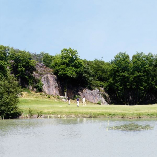 Golfbane med vand i forgrunden og store klipper i baggrunden