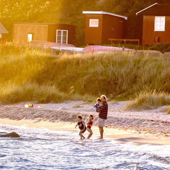 Far og tre børn står i vandkanten på Boderne strand