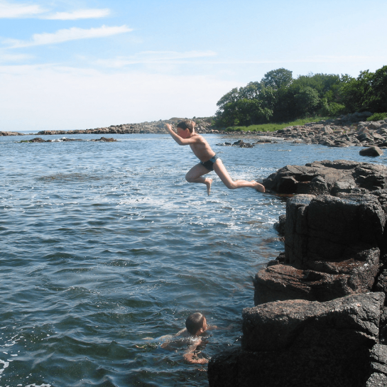 Barn hopper ud i havet fra klippe