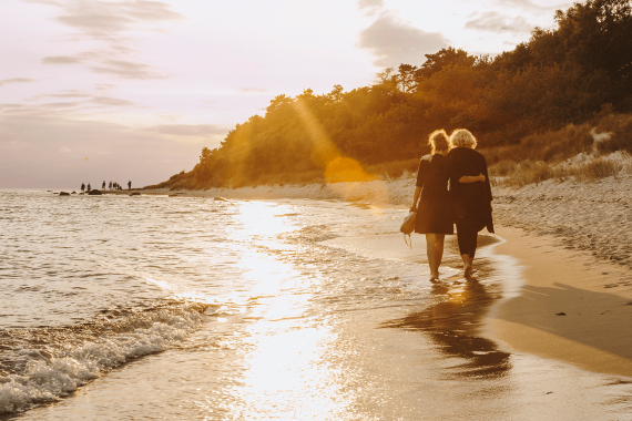 Par går ved siden af hinanden i vandkanten på stranden ved solnedgang
