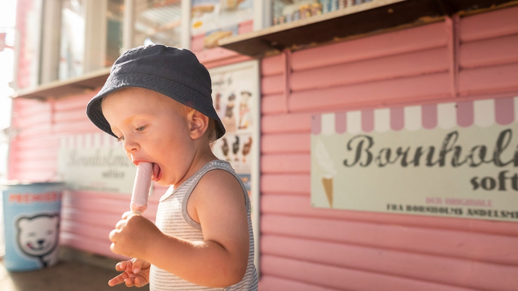 Barn med bøllehat spiser lyserød pind-is