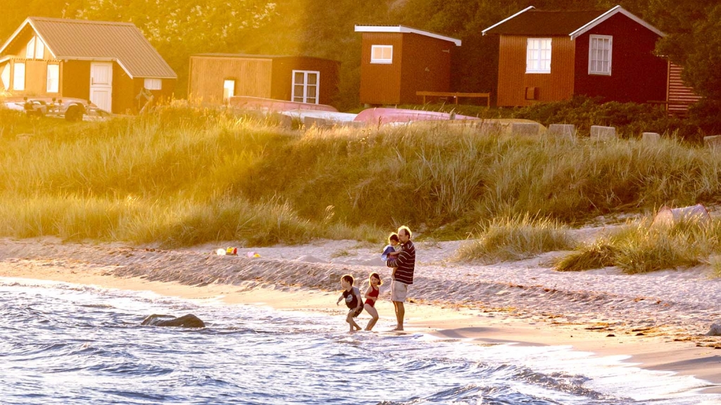Far og tre børn står i vandkanten på strand