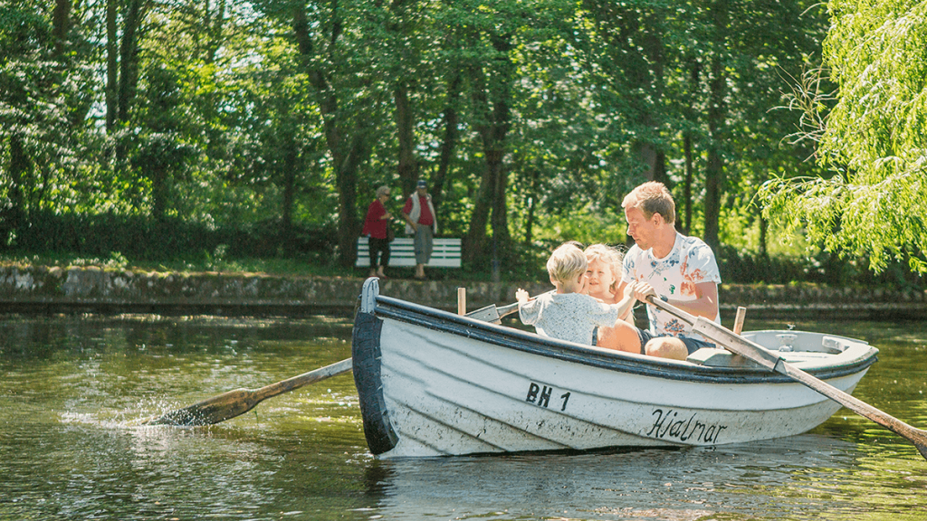 Far og to børn ror i en lille jolle på en sø
