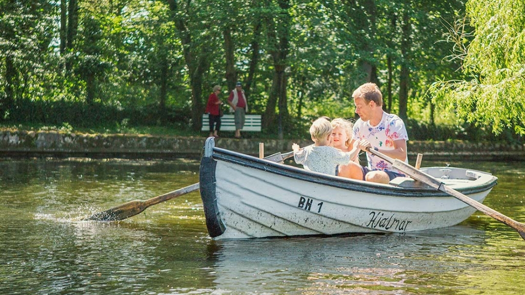 Far og to børn ror i en lille jolle på en sø