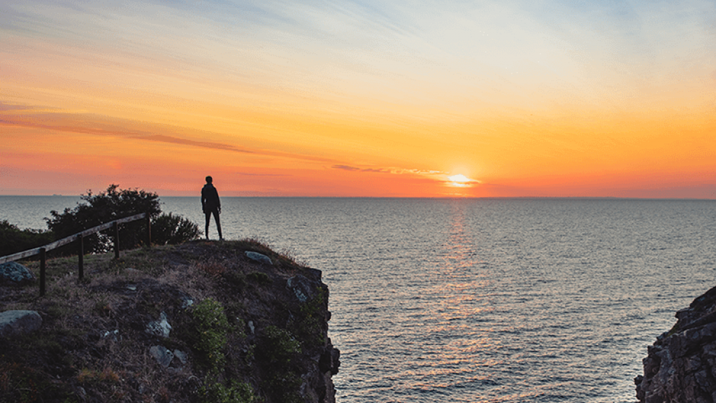 Person står på klippe og ser på solnedgang