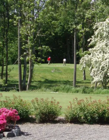 To personer står på en golfbane med grønne og lyserøde planter i forgrunden